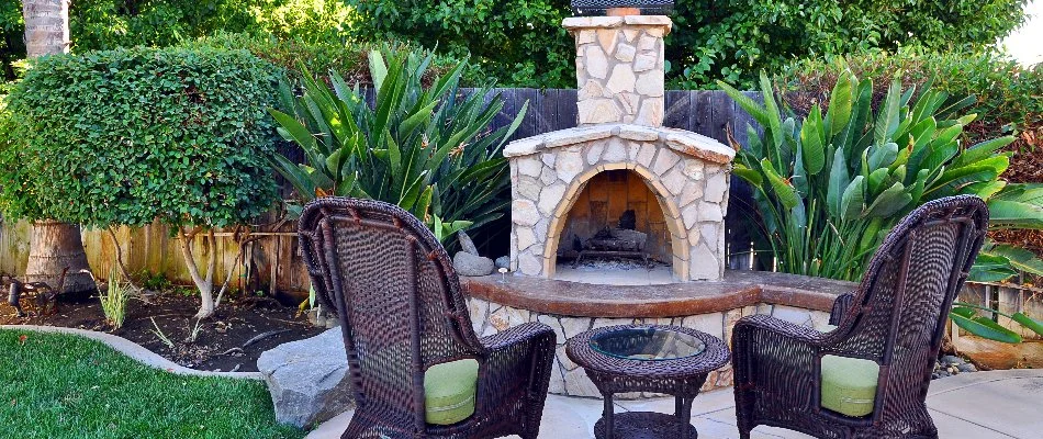 Stone outdoor fireplace with seating and beautiful greenery.